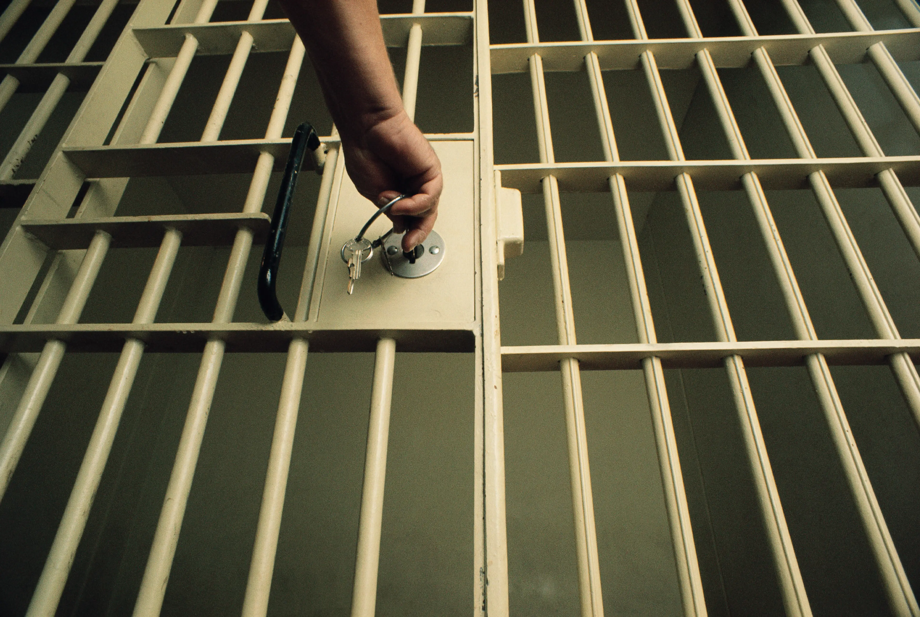 A photograph of a hand reaching out to lock a prison cell with a bunch of keys